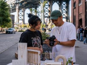 Creator and jewelry seller reviewing photos on a camera at an outdoor market near the Manhattan Bridge.