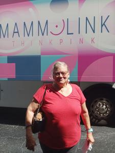 A patient poses outside the MammoLink mobile mammography bus after receiving her mammogram during the 2025 screening event.
