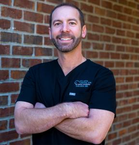Dr. Davis Smith, DMD, wearing black scrubs in front of a brick wall