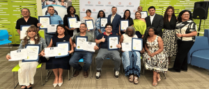 Group photo of diverse individuals proudly holding certificates during an indoor award or graduation ceremony.