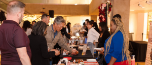 People interacting at a vendor table displaying various products inside a warmly lit event space.