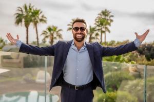 Amir Davidson, CEO of Davidson Real Estate, standing with arms open on the terrace of a luxury villa in Caesarea, Israel.