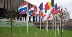 National flags of many countries flying on flagpoles outside a European institutional building.