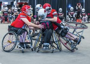 An Arizona Cardinals wheelchair football player with the ball gets tacked by two opponents