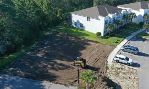 Aerial photo of a skid steer grading a cleared lot next to white townhomes and a parking lot.