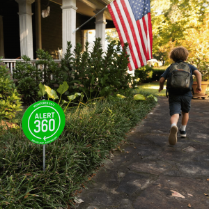 Boy with backpack running up to the front door of his home in the foreground there is an Alert 360 yard sign