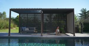 Mirador pergola equipped with shutter walls and a pull-down screen, creating a shaded and private outdoor living space beside a swimming pool.