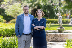 Palm Beach Accounting and Financial Services Senior Client Manager (Client Accounting Services) Joshua Nelson, CPA wears a blue-grey sport coat, tan slacks, and square-framed glasses. Standing next to him is PBAFS president Silvia Chestnut Evans, MBA, CPA