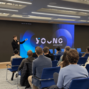 Timoté Chanut, founder of Young With Solutions, speaking to an audience at a presentation with the Young With Solutions logo displayed on screen behind him.