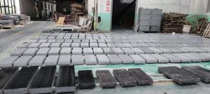 Rows of gray and black granite monument components arranged on a workshop floor for inspection.