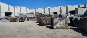 Large granite blocks stored outdoors beside stone-processing workshop buildings.