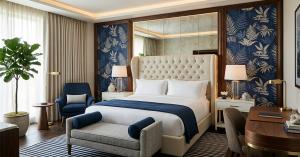 Luxury hotel guest room with a tufted bed, blue botanical wall panels, lounge chair, bench and wood desk.