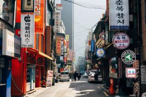 A bustling street in Seoul, South Korea, lined with colorful Korean business signs and pedestrians, illustrating the dynamic urban environment where F-2 and F-5 permanent residents settle and invest.