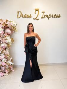 Woman wearing a black strapless evening gown with a bow detail and thigh-high slit at Dress 2 Impress boutique.