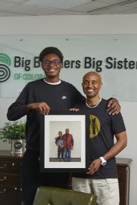 Imari & Spencer at the BBBSC office holding a photo showing the day they were first matched.