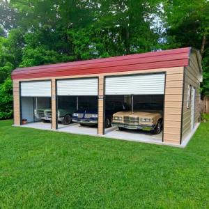 a clean exterior of a finished metal garage with three roll-up doors and three classic cars inside