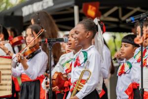 Young student in Mariachi attire is on stage with other students. She is smiling.