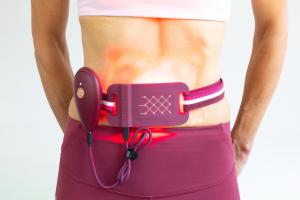 ILYEO body worn on a woman’s lower back with its red-light therapy LEDs illuminated.