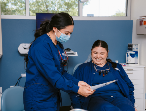 student in dental PPE shows paperwork to a fellow student sitting in the dental chair acting as the patient