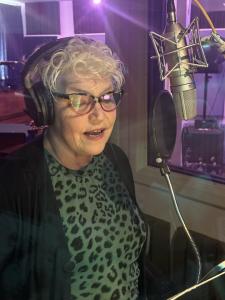 Kathy Coffey Solberg wearing headphones and speaking into a studio microphone while recording audio.
