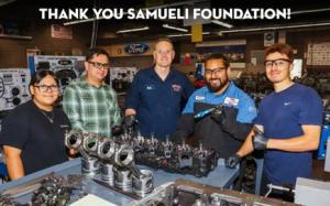 Automotive Technology students smile at the camera holding tools in their blue Automotive jumpsuits