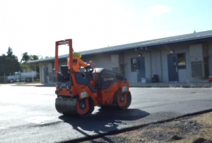 Asphalt compactor roller smoothing and compacting new pavement on a commercial property.