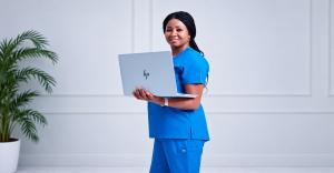 Blessing Dan-Dukor wearing blue scrubs and holding a laptop in a professional clinical portrait.