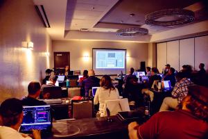 Post-production professionals working in editing software on laptops in a workshop room while an instructor presents on a large screen at Post|Production World.