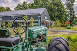 A vintage green tractor on the lawn in front of the gray Farmers Choice barn in New Paltz, with flags and bunting along the porch.