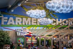 A red, white and blue model airplane and cloud-shaped lights hanging in front of a large Farmers Choice sign and a striped awning.