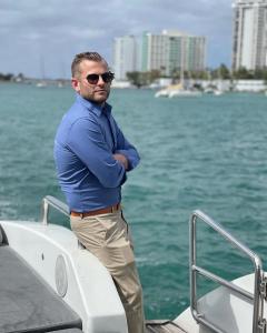 Justin Keeperman, founder of JustKeeps Travel, standing aboard a yacht in Miami with the waterfront skyline in the background.