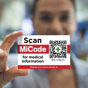 Close-up of a person holding a red and white MiCode wallet card displaying a QR code and the words “Scan for medical information”.