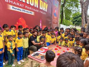 Adv. Peeyush Pandit seated among a large group of schoolchildren in yellow uniforms during an outdoor celebration of Swarna Bharat evillage Foundation Day.