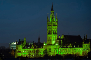 The University of Glasgow’s main building and tower illuminated bright green at night.