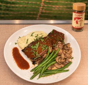 Meatloaf, mushrooms, green beans and mashed potatoes on a white oval plate next to a bottle of XXHEAT Chili Powder