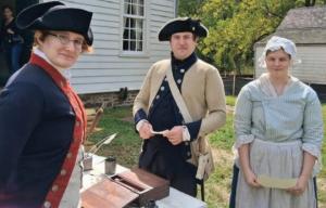 Two men and a woman in colonial dress outdoors