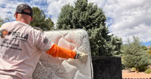 Bella Junk Removal crew member loading a mattress into a dump truck.
