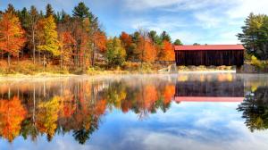 A red, covered bridge in Bartlett, New Hampshire USA, trees reflecting in the lake.