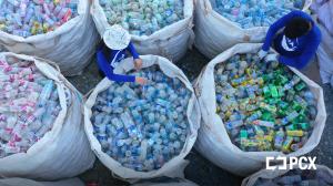 Two workers sort collected plastic bottles into large sacks at an ocean-bound plastic collection site in Cambodia.