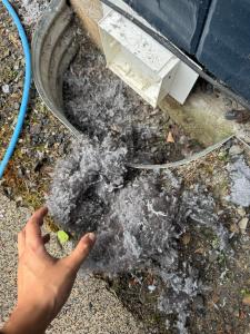 Lint beside an exterior dryer vent with a cleaning hose visible