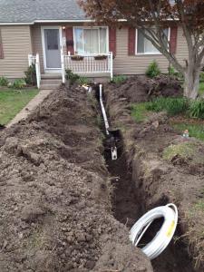 Open trench with new sewer pipe installed in front of a residential home