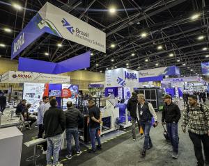 Vista del Pabellón de Brasil en una feria internacional del sector del plástico, con stands y equipos industriales en exhibición. En la parte superior del espacio, estructuras suspendidas muestran las marcas Brasil y Brazil Machinery Solutions. Diversos p