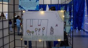 A drawing depicting a swing set with 6 sunflowers, the sun, a rabbit and a butterfly. A caption by the young artist says, "My art is about a park where can be happy, safe, and free. In my park, children can play in the flowers, laugh, and enjoy their toys
