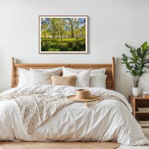 Green ICM abstract woodland fine art print displayed above a timber bed in a bright neutral bedroom with natural textures and indoor planting.