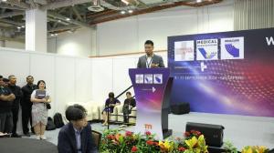 Zen Koh speaking at a podium in front of an event stage backdrop.