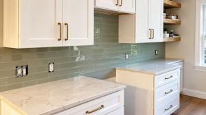 White kitchen cabinets with a green tile backsplash and gold hardware by A & R Remodeling and Construction.