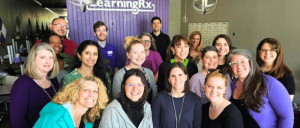 Group photo of 18 smiling adults standing indoors in front of a purple wall with "LearningRx" sign.