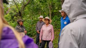 Coffee farmer Nancy Conde stands on a coffee farm in Ecuador surrounded by other people and lush green vegetation.