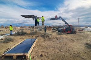 Workers install a solar array on a raised platform at Wind River, Wyoming, with a crane and additional panels staged nearby.