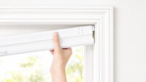 Hand installing TensionLock no-drill cellular shade inside window frame.